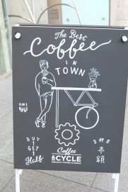 The Best Coffee in Town Buy 1 Get 1 Half Coffee and Cycle sign outside of Ratio Coffee & Cycle